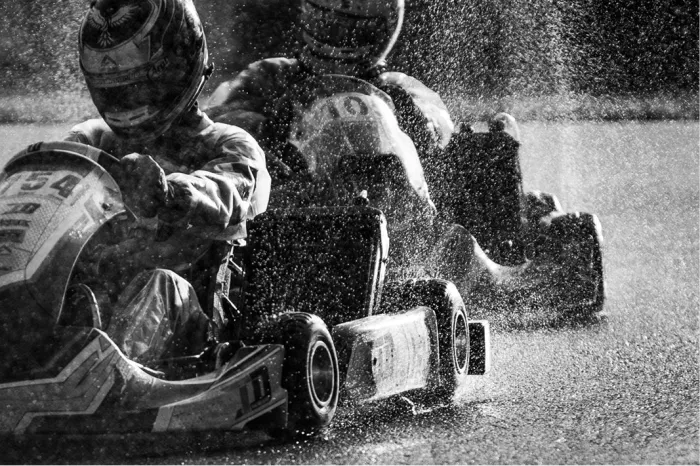 Twee karts naast elkaar in de regen tijdens een inhaalmanoeuvre in zwart-wit