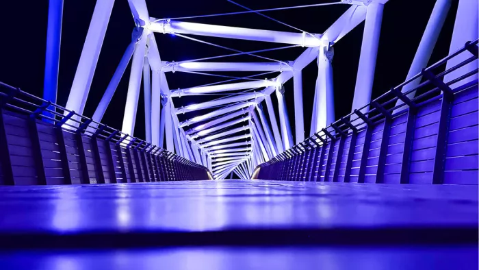 Blauw verlichte voetgangersbrug met witte stalen spanten bij nacht