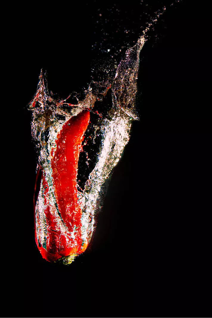 Rode paprika die in water valt met spetters en luchtbellen tegen een zwarte achtergrond