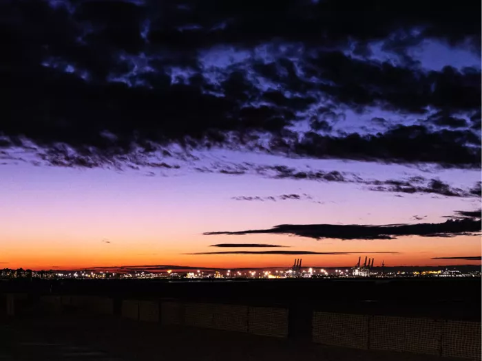Paarse en oranje avondlucht met donkere wolken boven een haven met verlichte kranen
