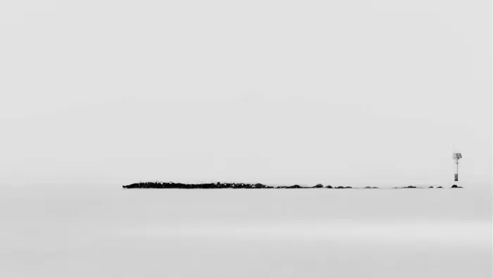Lage golfbreker met een navigatiepaal in een egaal grijze zee, minimalistisch in zwart-wit